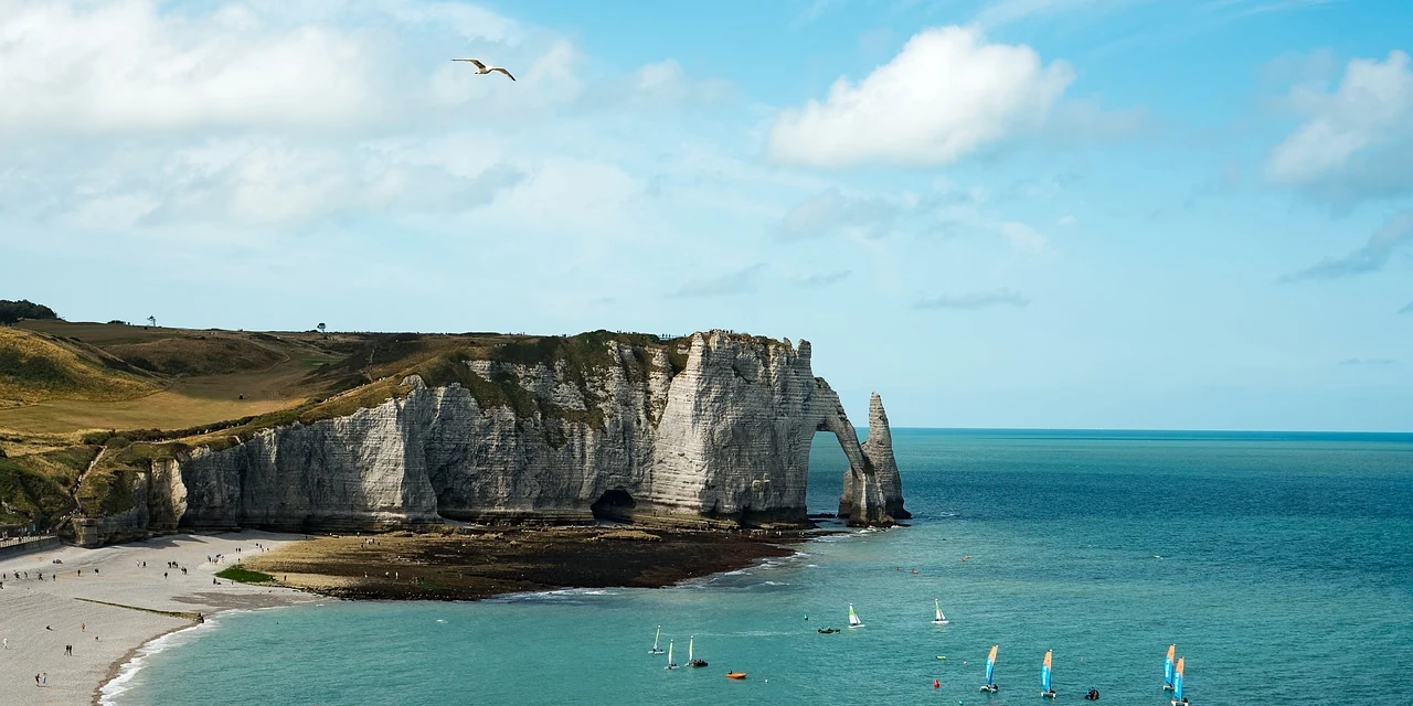 The arch and the Needle across the bay, sailboats on turquoise water, a long pebble beach